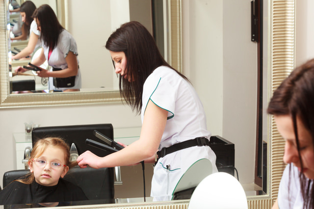 Hairdresser straightening hair little girl child in hairdressing beauty salon