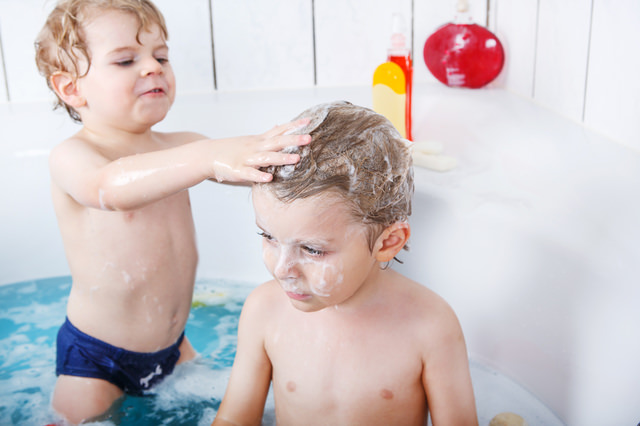 Two little twins boys having fun with water by taking bath in ba