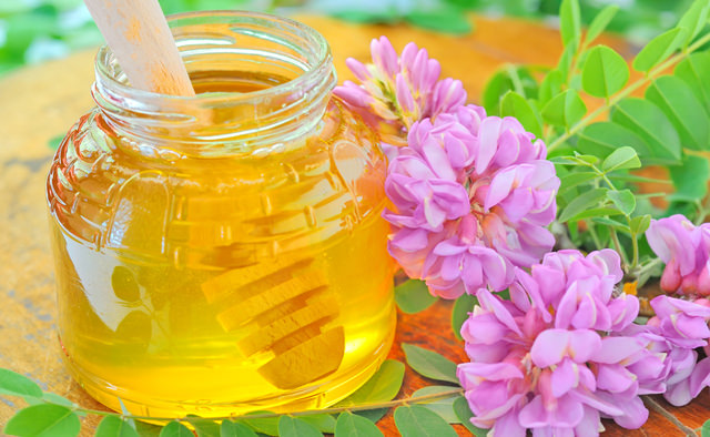 glass jar full of honey and stick with acacia pink and white flo