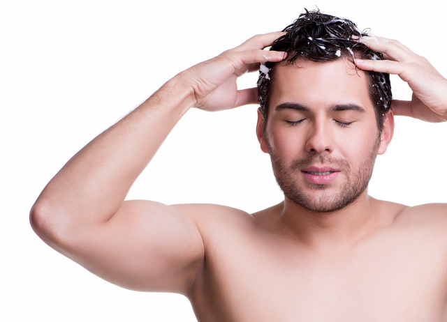 Young happy smiling man washing hair.