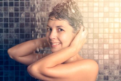 Frau massiert Shampoo in ihre Haare unter der Dusche